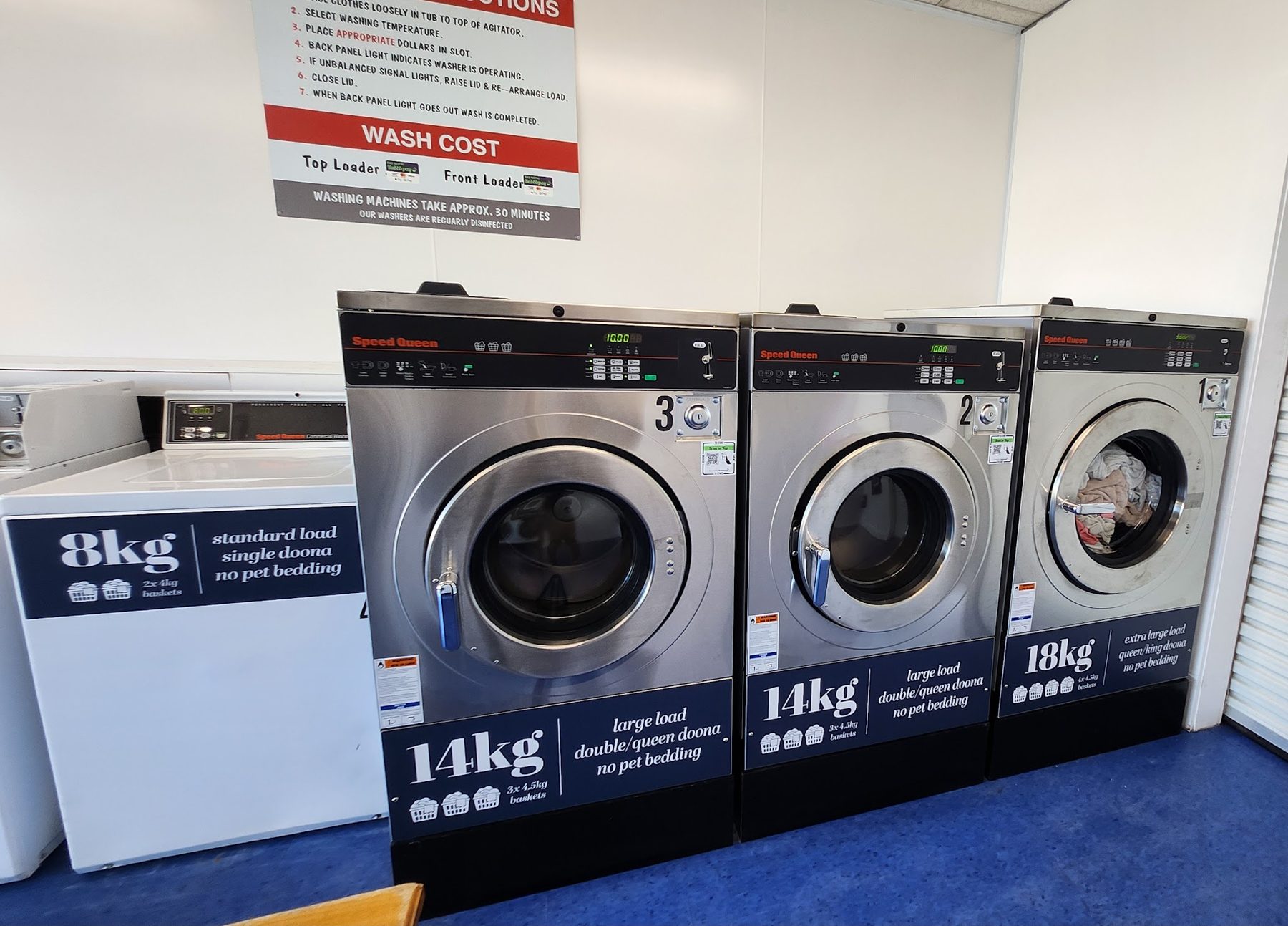 Row of stainless Speed Queen front-loading washers labelled 14kg and 18kg beside an 8kg top loader