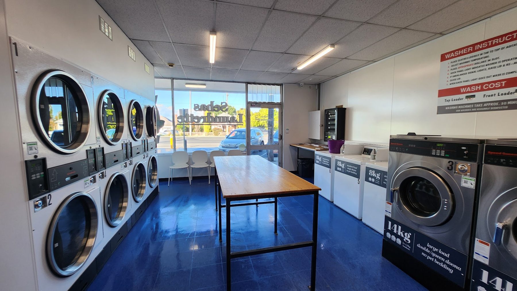 Inside Sebas Laundrette: a wall of dryers, the long folding table and seating by the front window